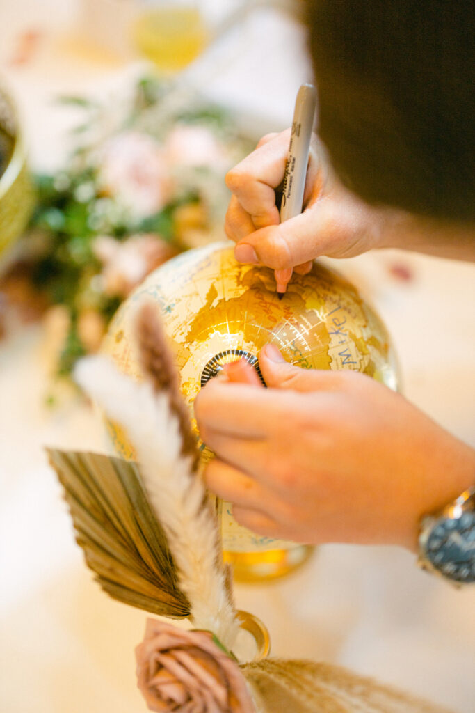 The wedding guests signing an antique globe instead of a guest book for a memorable wedding heirloom.