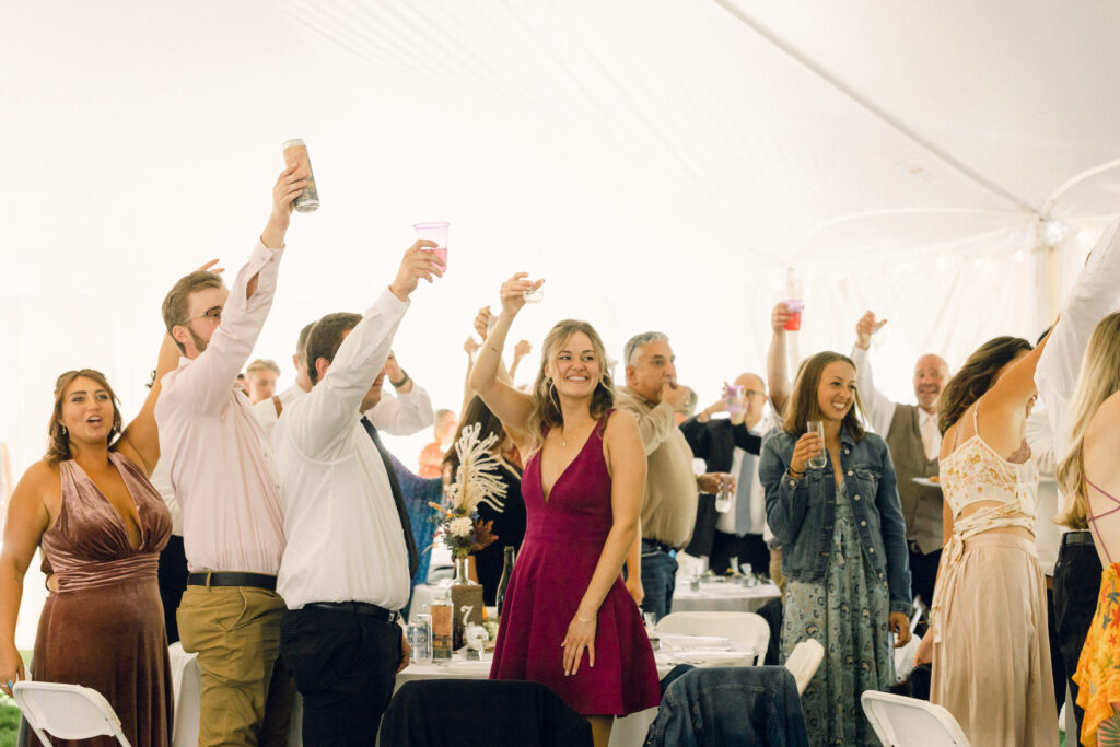 The wedding reception guests hold their classes in the air to toast.
