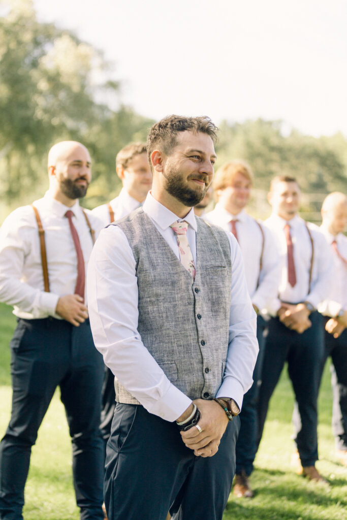 The groom smiling as the bride walks down the aisle in an outdoor wedding at Glen Brook Farm.