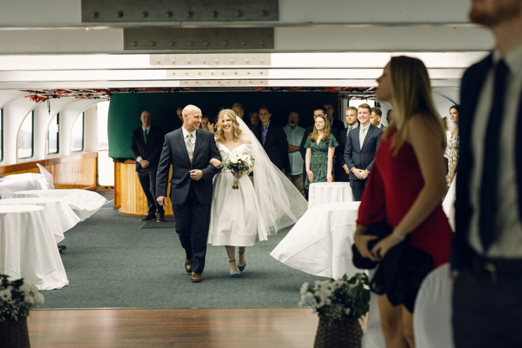 The father of the bride walks her down the aisle on the boat of Lake George wedding.