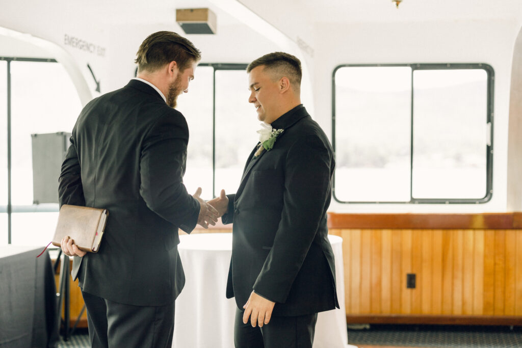 The groom and best man stand at the altar on the Lake George boat wedding and shake hands.