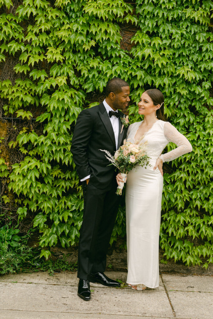 The bride and groom stand in front of greenery at an NYC park, taken by Molli Photo, New York City wedding photographer.