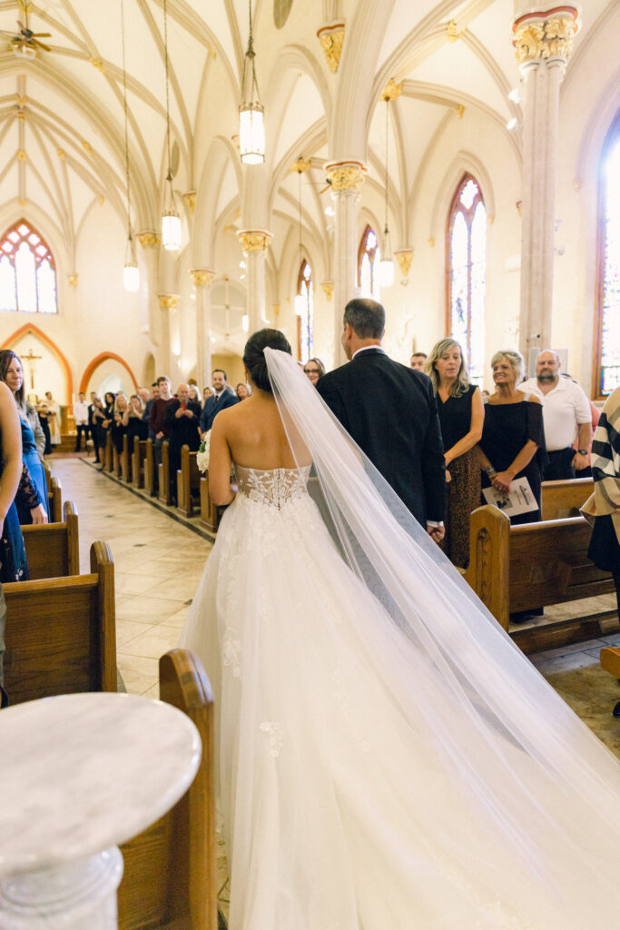 The bride walking down the aisle with a long, cathedral length veil. 