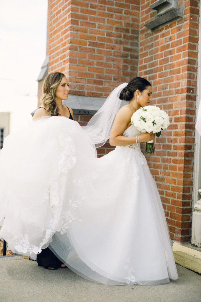 The maid of honor helps the bride into the cathedral at St. Mary's in Queensbury New York.