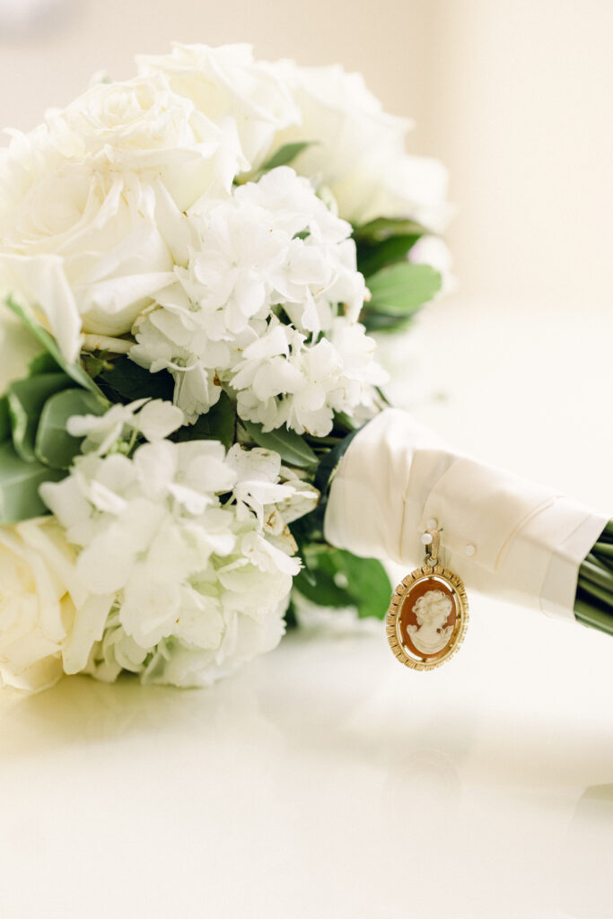 Bride's bouquet with white roses and white hydrangeas wrapped in ivory ribbon pinned using a family heirloom vintage pin.  