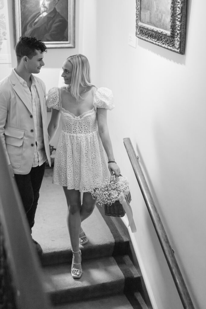 A couple walking down a staircase for engagement photos in an art gallery.