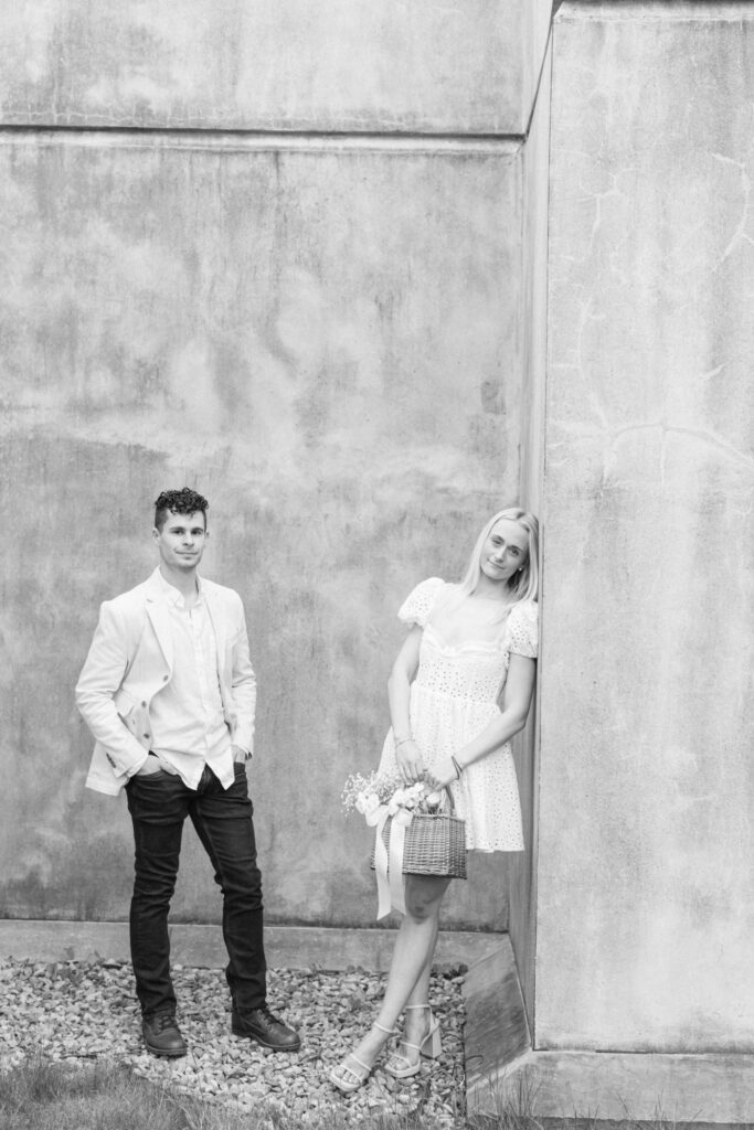 A couple stands against a concrete wall outside of an art museum for an engagement session.