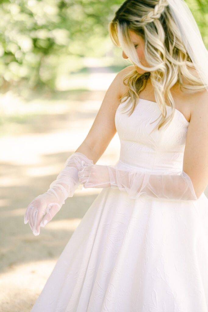 Bride adjusting her tulle gloves in a meadow. 