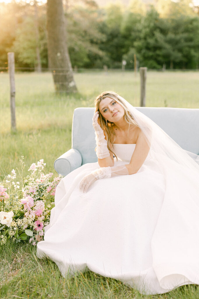 Bride looking into a meadow while sitting in a blue loveseat.
