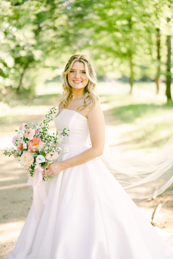 Bride smiling in a meadow while she holds a pink bouquet. 