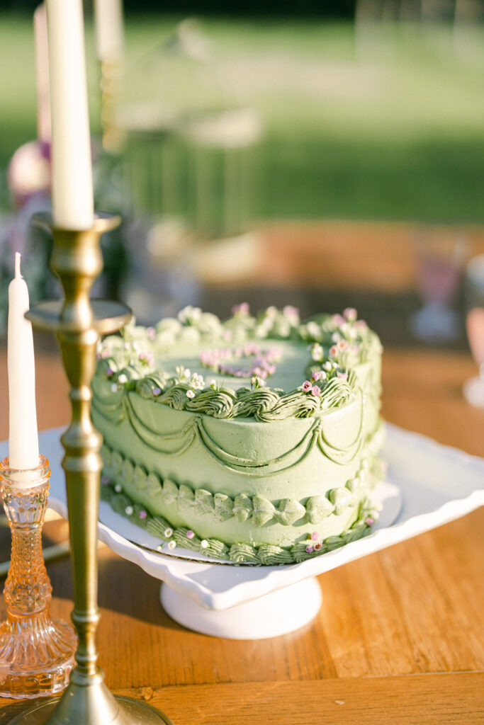 Garden party wedding cake with green icing, a heart shape, and pink and white details.