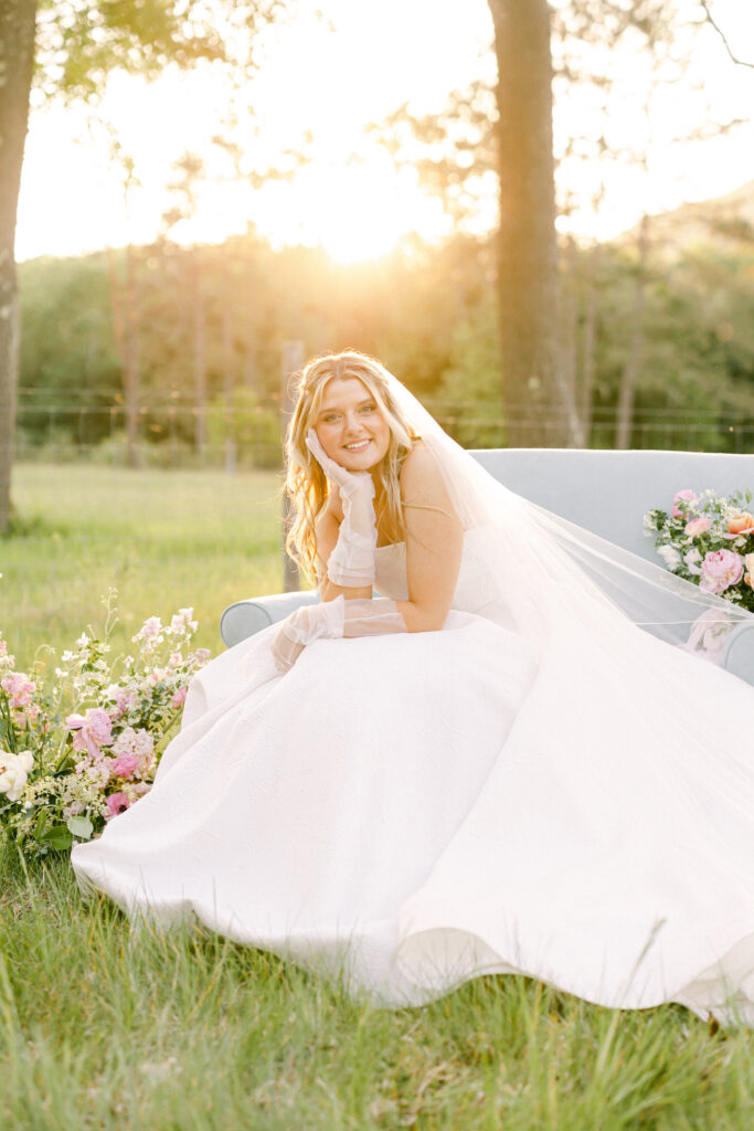 Bride smiling as she sits on a blue loveseat at a garden party wedding.