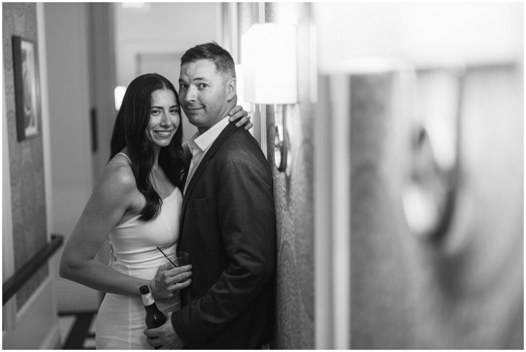 Newlyweds smile and lean against a wall with their drinks at their the adelphi hotel wedding