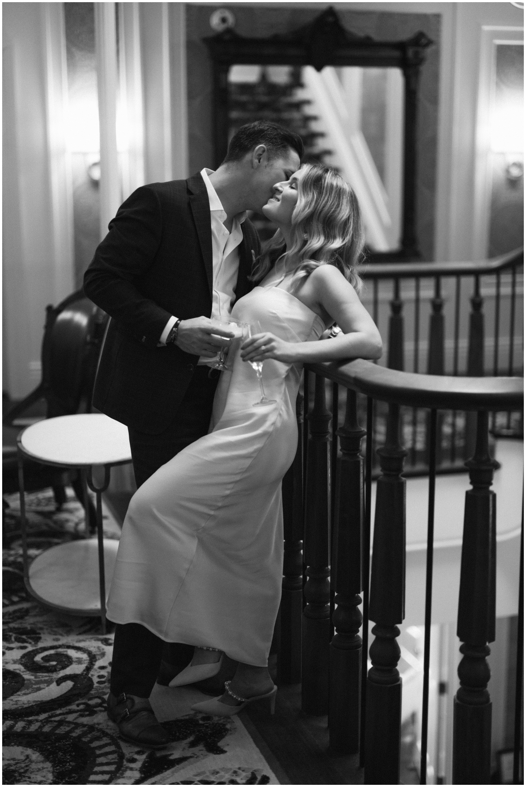 A groom kisses the cheek of his smiling bride as she leans on a wooden banister at the adelphi hotel wedding venue