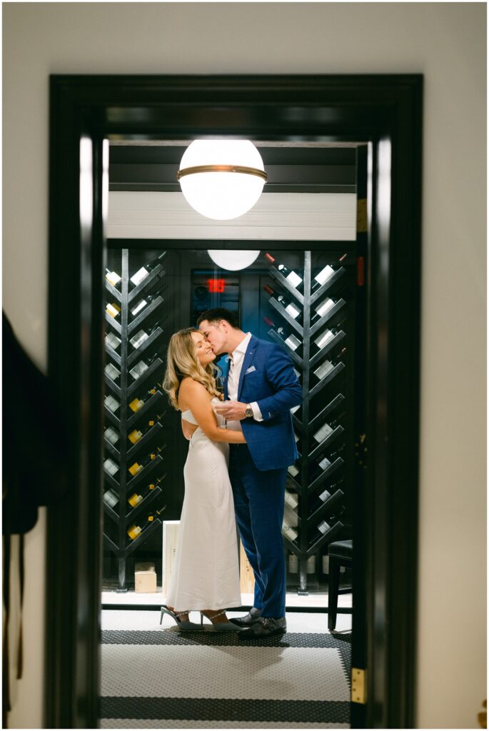 A bride smiles while her groom kisses her cheek in the wine cellar at the adelphi hotel wedding venue