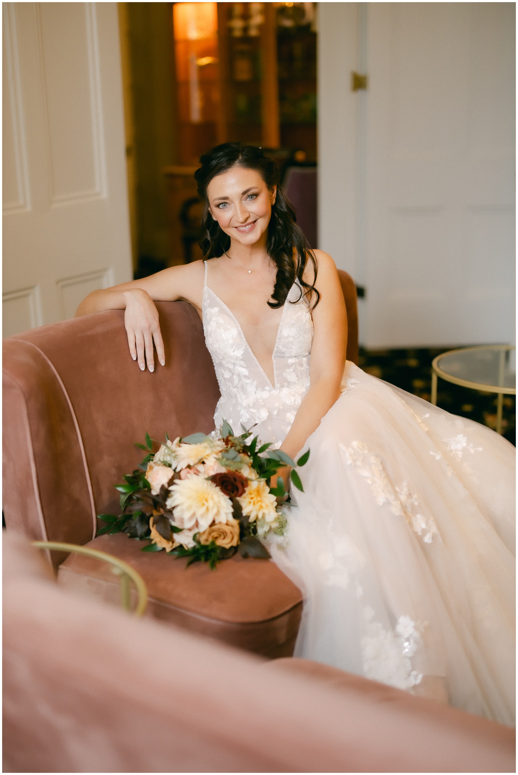 A bride smiles while sitting in a chair in her getting ready room