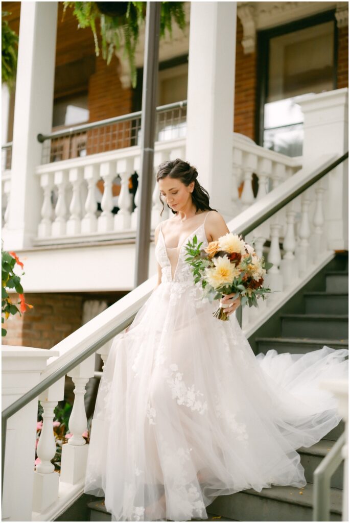 A bride walks down the steps of the mansion of saratoga holding her colorful bouquet