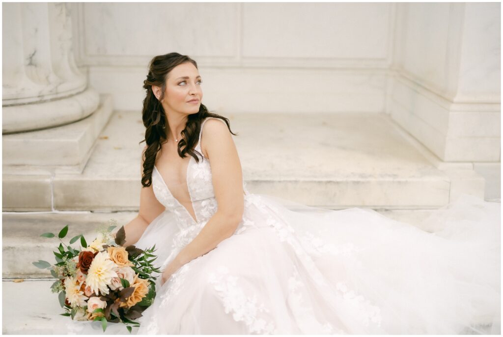 A bride sits on the steps looking over her shoulder with her bouquet