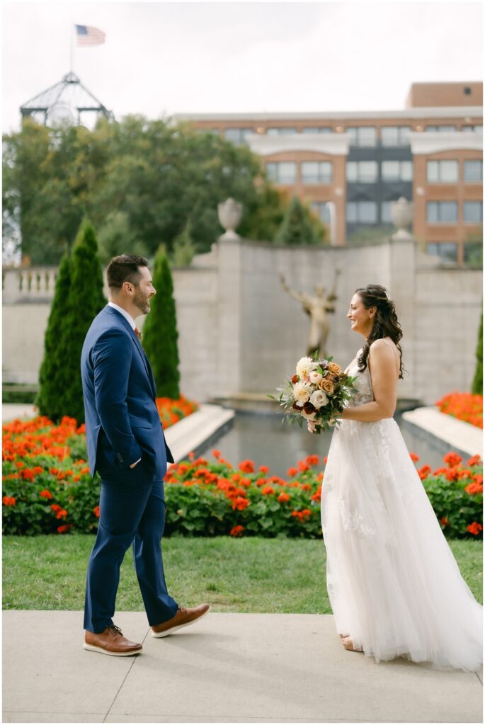 A bride and groom smile at each other in the gardens by ponds at their wedding at the mansion of saratoga