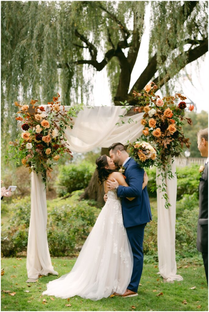 Newlyweds kiss under the arbor to finish their wedding ceremony under a willow tree at the mansion of saratoga