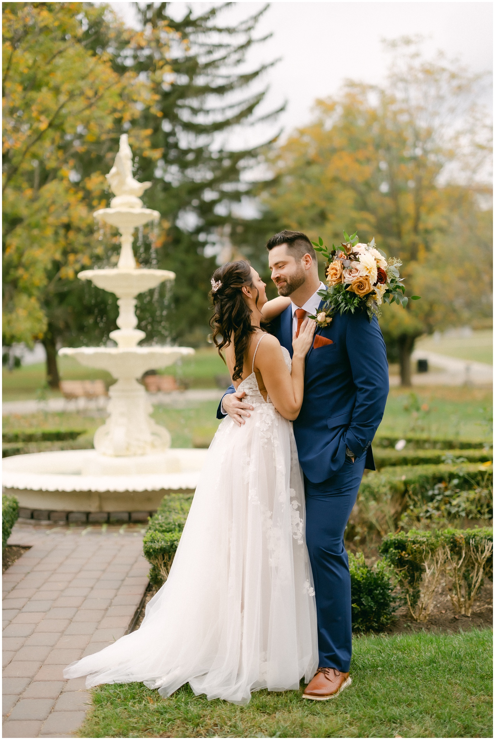 A bride and groom stand by the garden fountain embracing at the mansion of saratoga